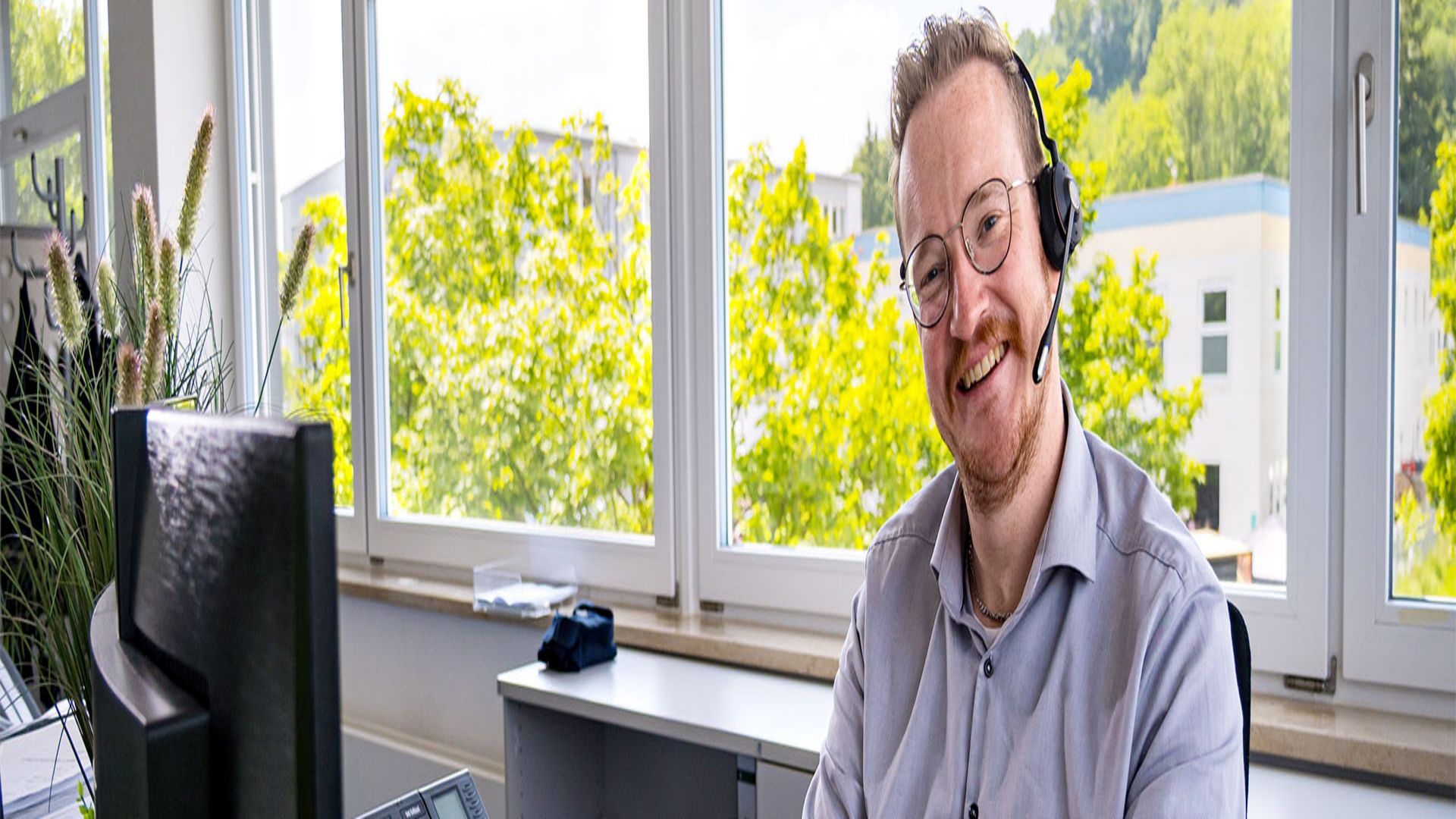 Mitarbeiter sitzt vor seinem Monitor am Schreibtisch und l&auml;chelt