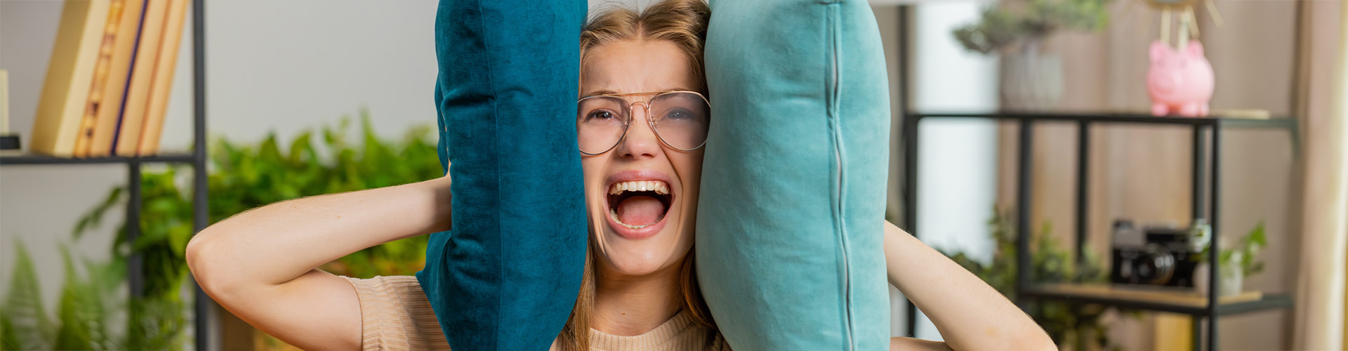 Frau hält sich mit Kissen die Ohren zu und schreit